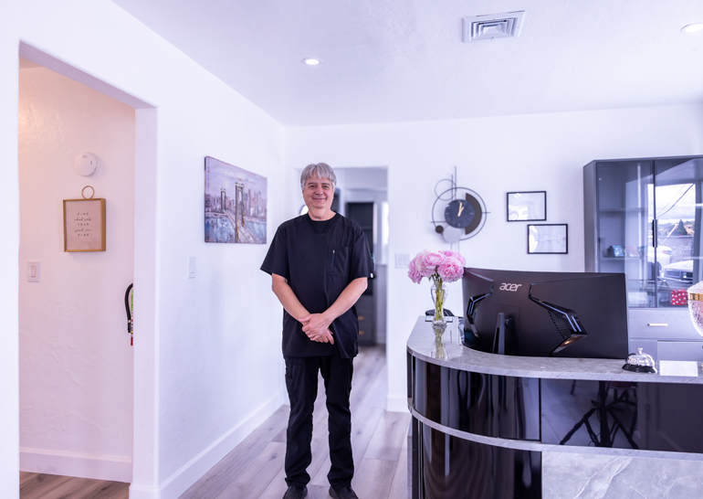 Smiling man in modern dental office. Denturist Randall Clasen in black scrubs creates the most natural smiles in Roseburg.