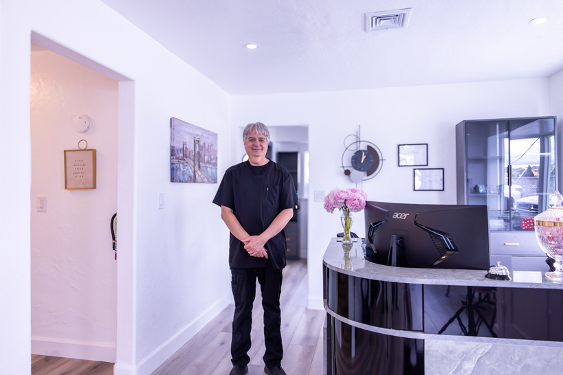 Smiling man in modern dental office. Denturist Randall Clasen in black scrubs creates the most natural smiles in Roseburg.
